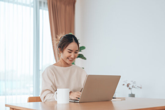 Beautiful young Asian woman working with laptop computer in living room. Work at home