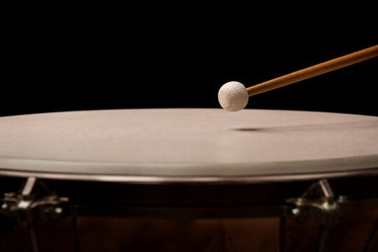 Drumstick poised just above the skin of a timpani drum.