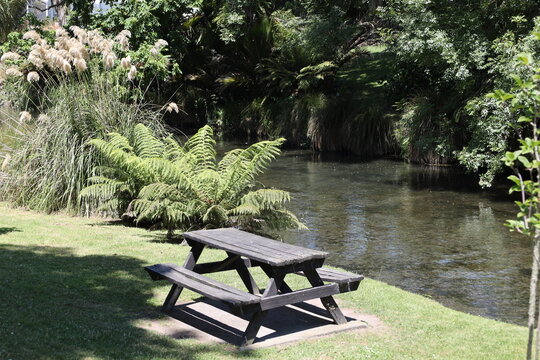 classic black-stained A-frame wooden picnic table set on grassy bank beside a stream (wide-angle, panorama, sunshine) 6157