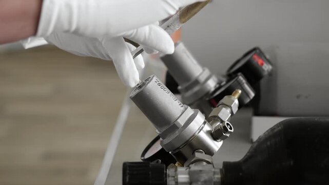 Laboratory technician in protective gloves adjusts a gas regulator with a hex key on laboratory gas equipment during technical setup and maintenance.