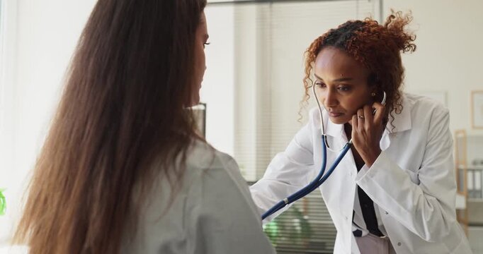 Doctor listens to patient with stethoscope during checkup. At the clinic the doctor performs examination and monitors heart, lungs and vitals. Medical consultation and diagnosis concept image.