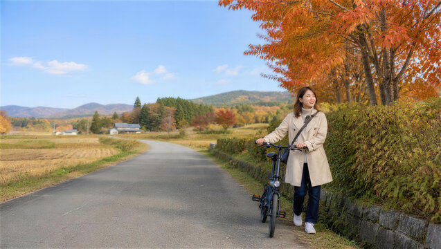 秋の農村で自転車を押す女性