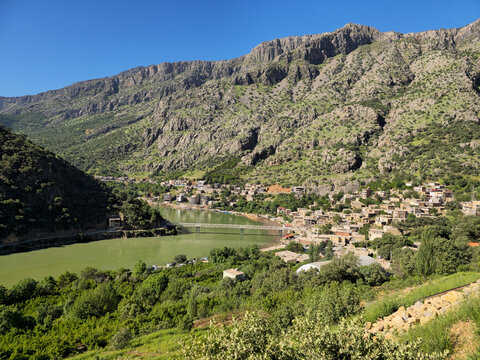 Mountain village clusters beside a calm green river, terraced houses and a bridge framed by rugged rocky cliffs above.
📍Selin village, Hawraman Takht, Kurdistan 