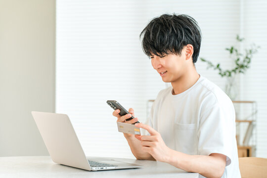 A young Asian man is holding a credit card and operating his smartphone.