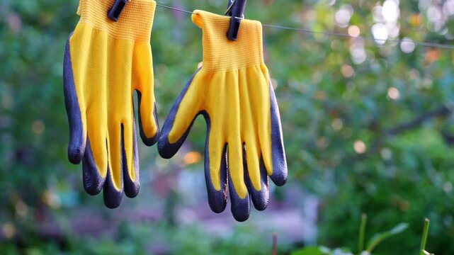 Yellow garden gloves tools dry on rope on greenery outdoor background during sunset. Spring summer gardening season. Concept of hand care hygiene and protection. Housework farm equipment