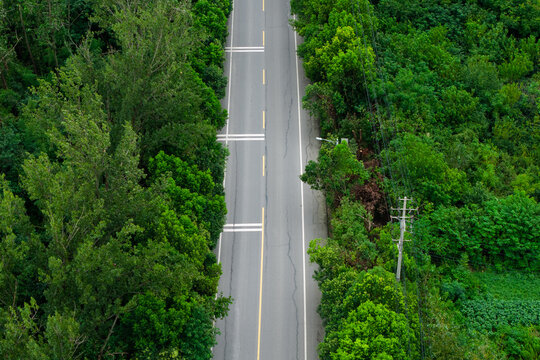 Aerial top view of rural asphalt road surrounded by dense green trees
