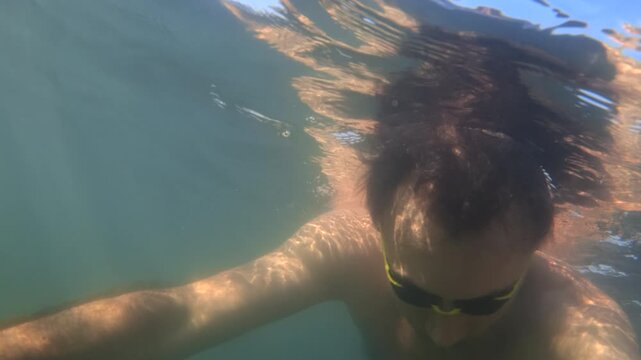 Man swimming underwater in clear blue water, sun rays penetrating surface. Leisure activity, summer vacation, aquatic sports