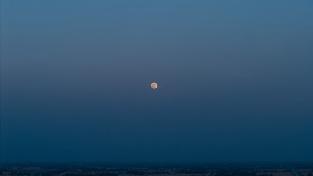Full moon in deep blue twilight sky over distant landscape