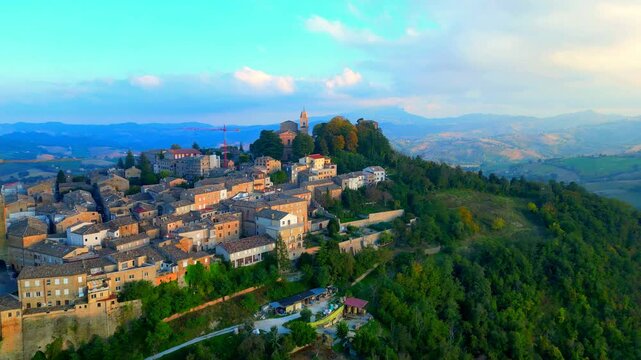 Sumptuous aerial truck right push-in shot from Santa Vittoria in Matenano, the town centre and its vintage buildings opening to a vision of a green promontory, full of thickets, typical Marche hills
