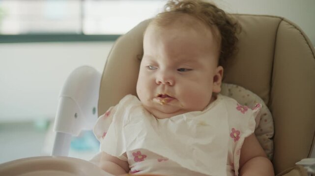 Baby with messy face and bib sitting in a high chair, exploring food during mealtime. Early childhood feeding concept