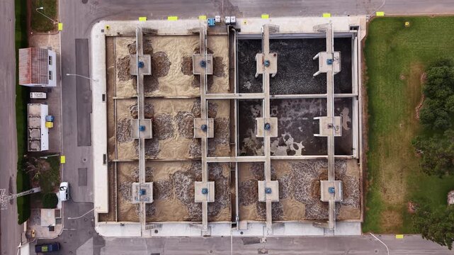 Overhead view of aeration basins at a modern wastewater treatment plant showing activated sludge process with mechanical aerators churning brown and dark water