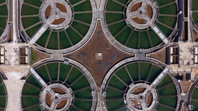 Overhead view of circular flocculation clarifiers connected by radial walkways at a drinking water treatment facility, forming geometric patterns with green water