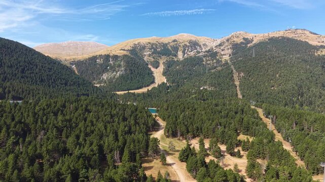 La Molina ski resort in the Pyrenees, Spain, during summer with dense pine forests, ski slopes, chairlift, small lake, and rocky mountain peaks under blue sky