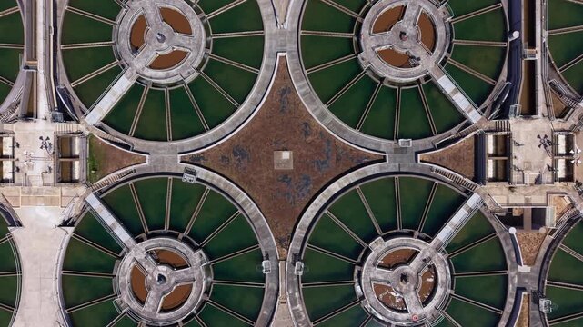 Overhead view of circular flocculation clarifiers connected by radial walkways at a drinking water treatment facility, forming geometric patterns with green water