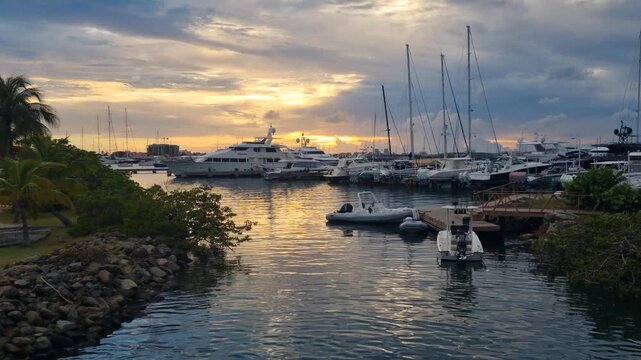 Calm sunset over Simpson Bay in St. Martin, with yachts moored in the harbor as the sun sinks behind a cloudy horizon, casting warm reflections across the tranquil water