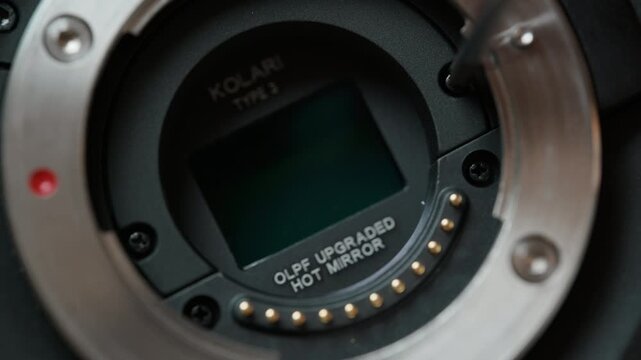 Close-up of the half-circle retaining bracket being screwed back down to secure the new IR cut filter over the sensor of a cinema camera. The final step of a camera modification, closing the sensor st