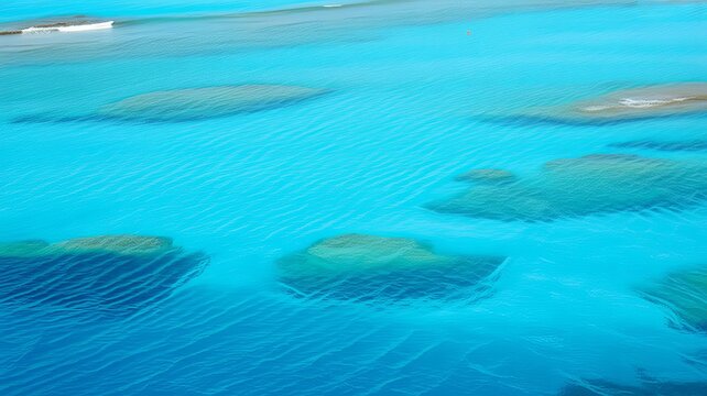 Aerial view of clear turquoise tropical ocean water with sandy patches and underwater rock formations visible through the shallow sea surface