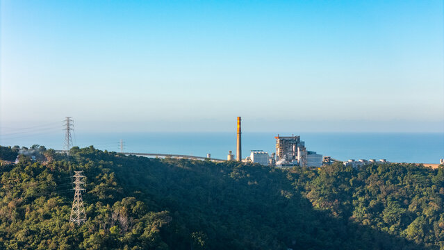 Aerial view of a seaside power plant with tall stack and ocean, symbolizing energy infrastructure, industry and future sustainability.