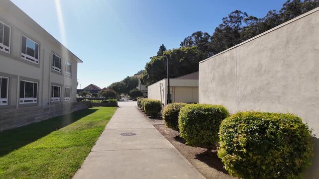 Point of view shot walking along a concrete pathway between buildings on the California State University Maritime Academy campus in Vallejo under a bright, sunny blue sky