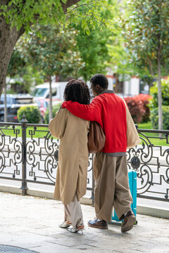 Stylish african american tourists with suitcase hugging and walking on street together, carefree black man and woman travelers enjoying each others company while walking to hotel from station. 