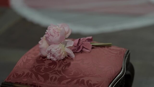 Pink peony flowers resting on red damask patterned cushion with dark wood frame