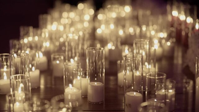 Rows of white pillar candles in clear glass cylinders creating warm bokeh glow