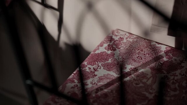 Red and white floral print fabric seen through dark iron railing in moody light