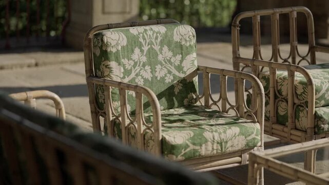 Vintage rattan armchair with green and white floral cushion on sunny stone terrace