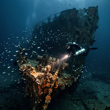 Scuba diver explores sunken shipwreck teeming with small fish underwater