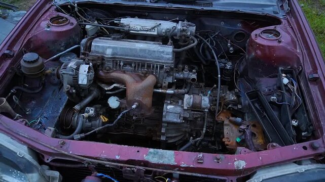 Old car engine bay with rusted components and mechanical parts under the open hood.