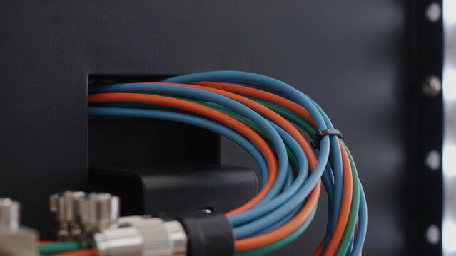 Network cables bundle in blue, orange, and green colors securely tied with black zip tie into network switch port.