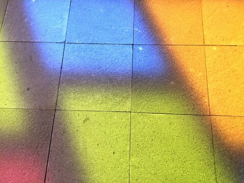 The projections of blue, green, yellow, and pink light from stained glass cast by sunlight falling onto the floor surface of a room