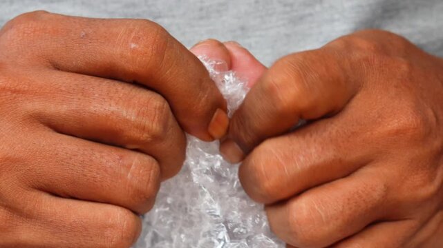 Man&rsquo;s hands squeezing and popping plastic bubble wrap at home for stress relief.