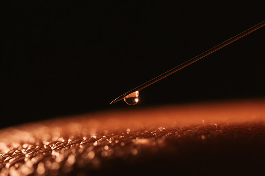 Dramatic low-angle photo of a hypodermic needle preparing for injection under overhead surgical lights