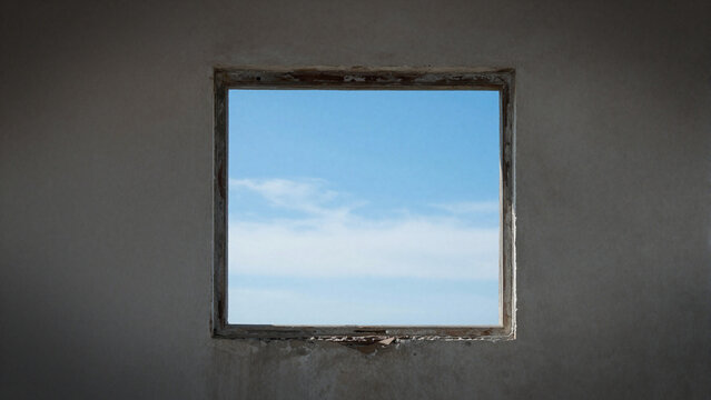 Simple square window on a weathered concrete wall framing a clear blue sky with white clouds