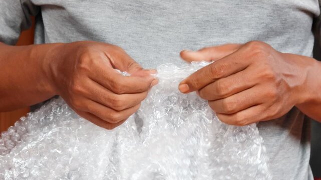 Man&rsquo;s hands squeezing and popping plastic bubble wrap at home for stress relief.