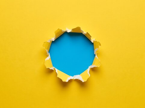 Torn hole in yellow paper revealing blue background