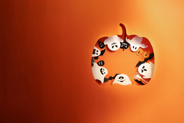 Halloween pumpkin paper cutout with ghosts and bats on orange background