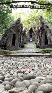Slow motion vertical video from a low angle showing a cobblestone path leading to a traditional village with rustic thatched roof huts. A distant hiker walks away. Cultural nature travel concept.