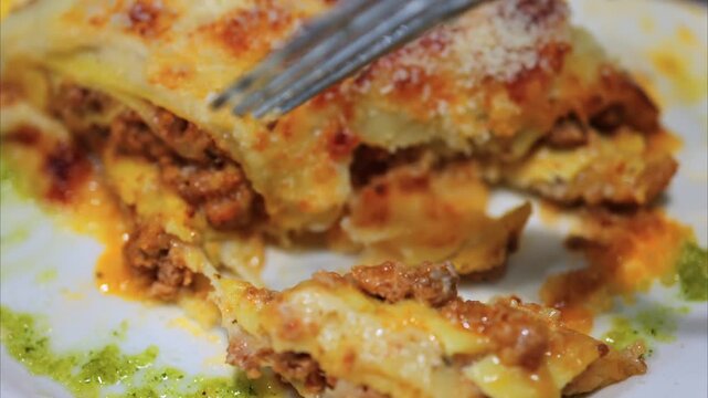 Close up shot of a fork taking a bite of delicious cheesy lasagna on a plate.