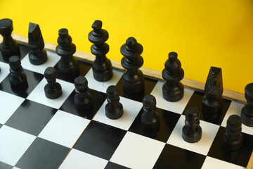 Black wooden chess pieces lined up on checkered chessboard with vibrant yellow background, strategic thinking, leadership, planning, and competitive game concept. © Nungkysoer