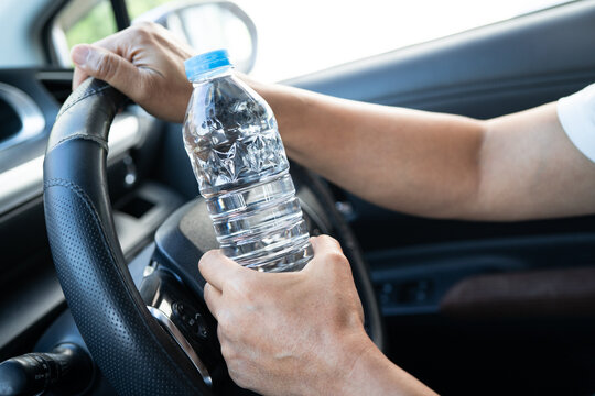 Asian woman driver holding bottle for drink water while driving a car. Plastic hot water bottle cause fire.