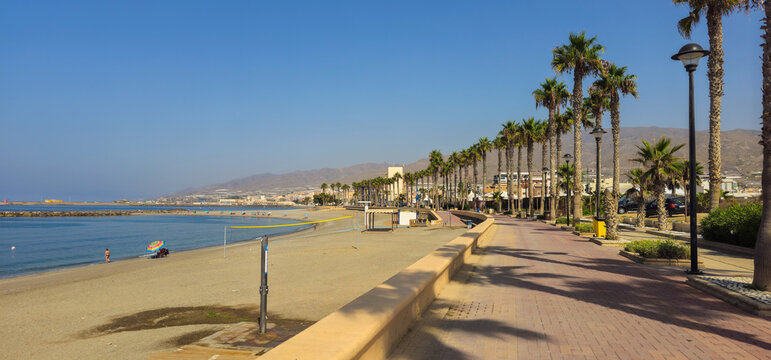 Palm lined beachfront promenade beside a Mediterranean beach with volleyball court, calm sea and mountain backdrop in Almu&ntilde;&eacute;car, Costa Tropical, Spain