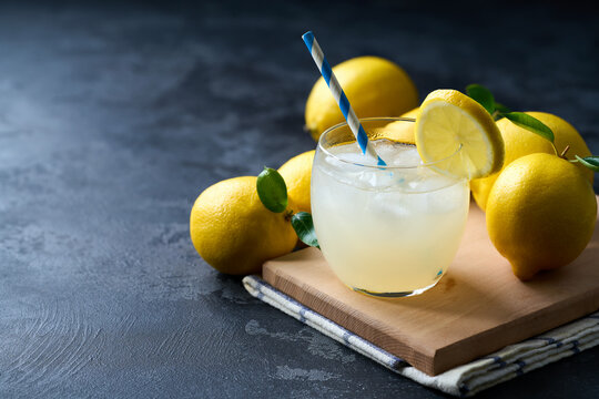 Glass of freshly made lemonade with ice on dark table, selective focus.