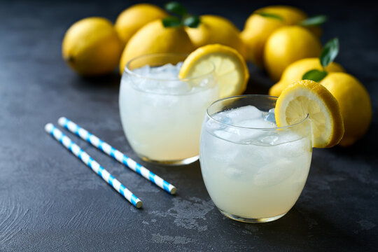 Lemonade with fresh lemon in glasses on dark background. Cold refreshing lemonade for summer party and fun.