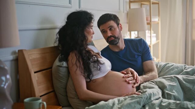 Expectant mother partner resting bed. Married couple touching baby bump bedroom.