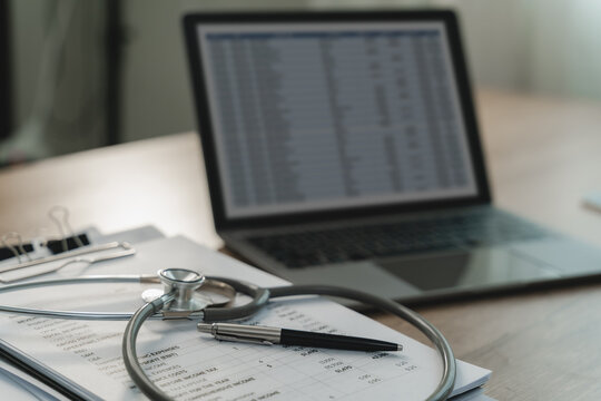 Stethoscope resting on a printed financial report beside a pen, tablet and laptop spreadsheet, illustrating healthcare financial analysis, medical expense review and reporting workflow.