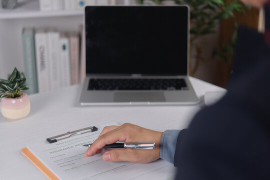 Patient hand filling medical health insurance claim form at desk with laptop