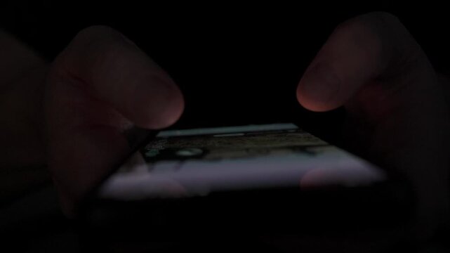 Close Up of Man Scrolling Social Media on Smartphone in Dark Room at Night