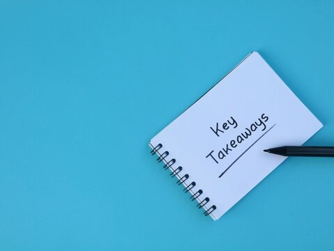 Handwritten text key takeaways on white book with pen on blue background with copy space. Ideal for business summary, learning point, strategy note, lesson learned, and corporate concept